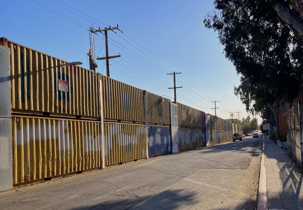 A row of shipping containers stacked two high on a neighborhood street recedes into the distance